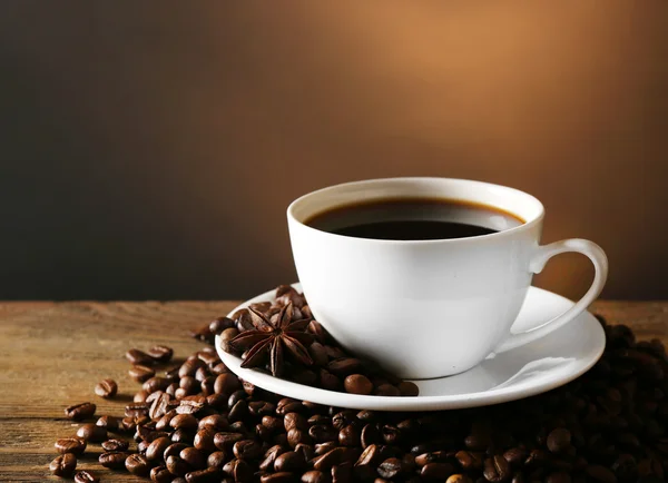 Tasse de café avec des grains sur table en bois sur fond sombre — Photo