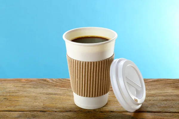 Paper cup of coffee on wooden table on blue background — Stock Photo, Image