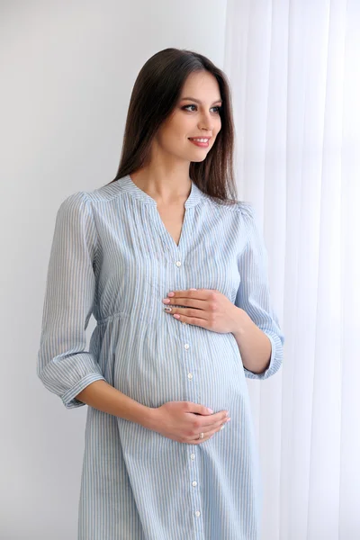 Gravid kvinna på vit vägg bakgrund, inomhus — Stockfoto