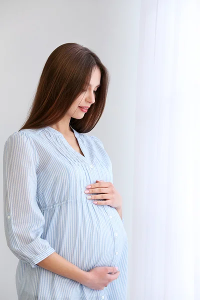 Mujer embarazada sobre fondo blanco de la pared, en interiores — Foto de Stock