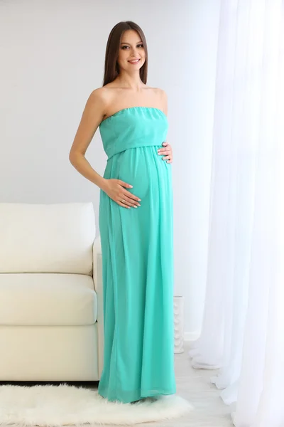 Pregnant woman standing near sofa in room — Stock Photo, Image