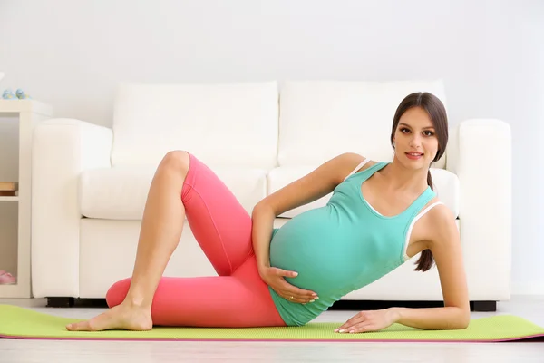 Mulher grávida se exercitando no tapete verde no quarto — Fotografia de Stock