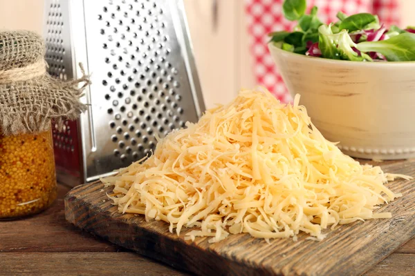 Grated cheese on wooden cutting board in kitchen — Stock Photo, Image