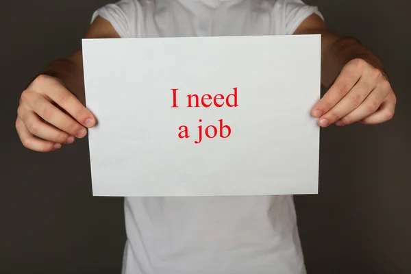 Sheet of paper with inscription I need a job in male hands on dark background — Stock Photo, Image