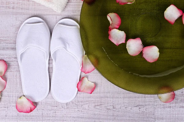 Wellnessschale mit Wasser, Rosenblättern, Handtuch und Hausschuhen auf hellem Hintergrund. Konzept der Pediküre oder natürlichen Wellness-Behandlung — Stockfoto