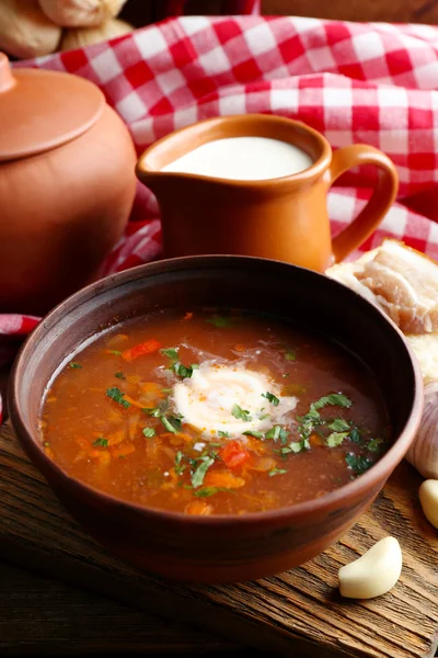 Soupe de betteraves ukrainienne - bortsch dans un bol et une casserole, sur une serviette, sur un fond en bois — Photo