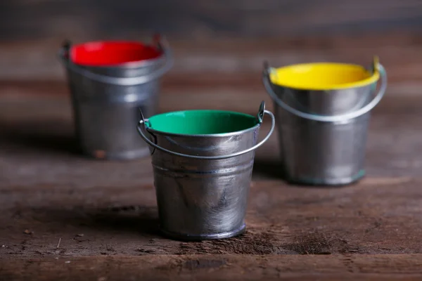 Metal buckets with colorful paint on wooden background — Stock Photo, Image