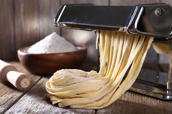 Hacer fideos con máquina de pasta sobre fondo de madera — Foto de Stock