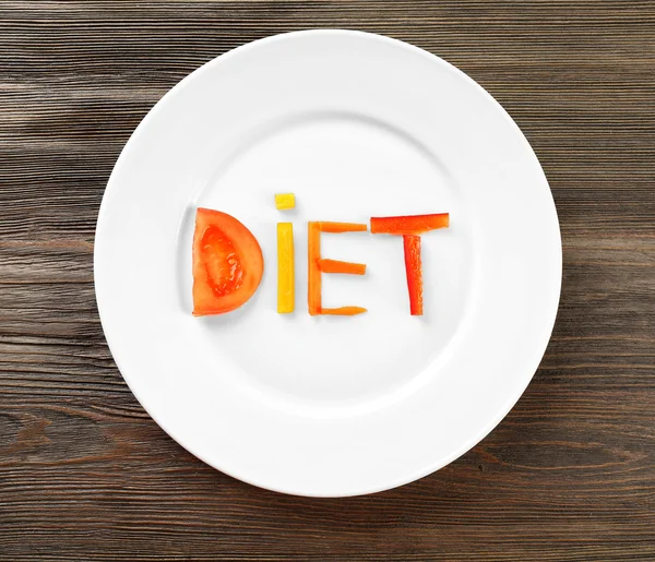 Slovo dieta vyrobené z nakrájené zeleniny v bílé desky na dřevěný stůl, pohled shora — Stock fotografie