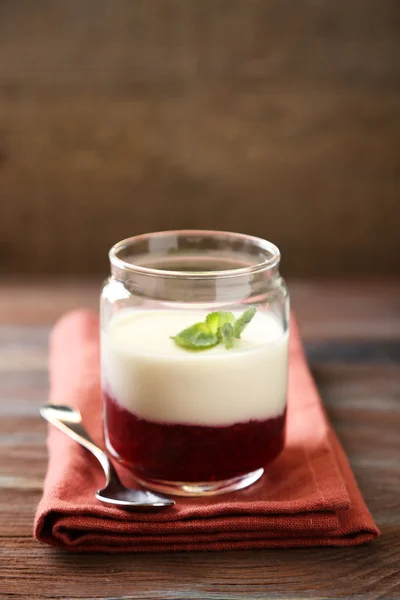 Glazen pot met smakelijke panna cotta dessert op bord, op houten tafel — Stockfoto
