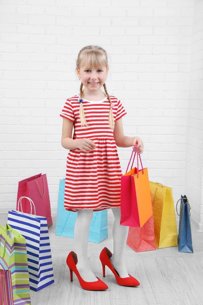 Vakker liten jente i mammas sko med handleposer i rommet. – stockfoto