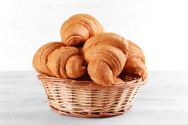 Croissants deliciosos na cesta de vime na mesa close-up — Fotografia de Stock