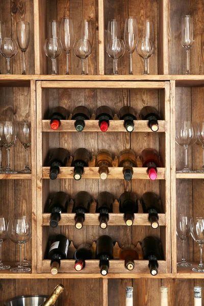 Shelving with wine bottles and glasses on wooden wall background — Stock Photo, Image