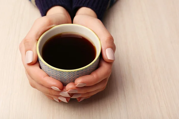 Ženské ruce držící šálek kávy na dřevěné pozadí — Stock fotografie