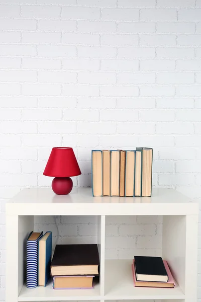 Wooden shelf with books and lamp on brick wall background