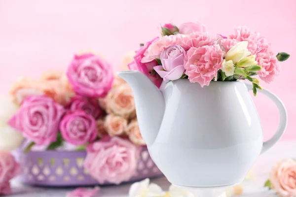Composition with beautiful spring flowers in teapot on light pink background — Stock Photo, Image