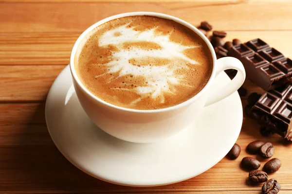 Cup of coffee latte art with grains and chocolate on wooden table, closeup — Stock Photo, Image