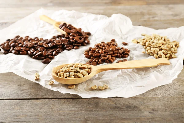 Kaffebönor på skrynkliga pergament på träbord, närbild — Stockfoto