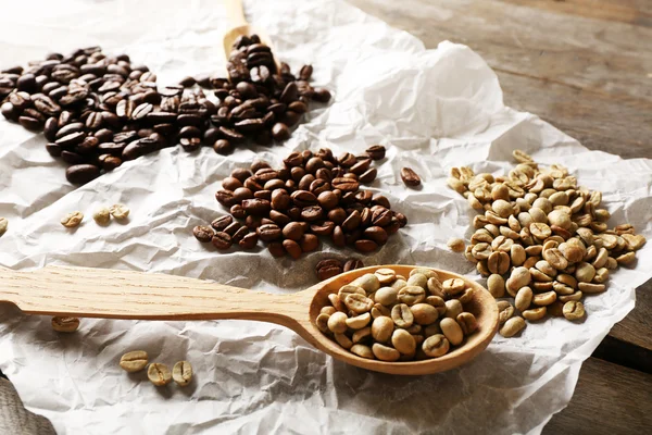 Grãos de café em pergaminho amassado em mesa de madeira, close-up — Fotografia de Stock