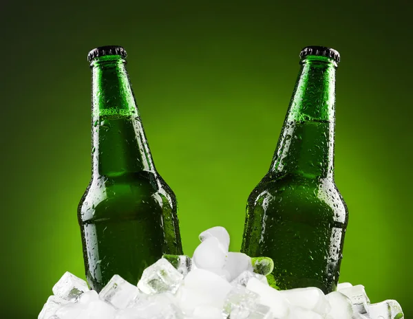 Glazen flessen bier in ijsblokjes op kleur achtergrond — Stockfoto