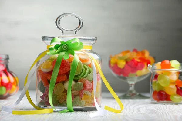 Bonbons colorés dans des pots sur la table sur fond en bois — Photo