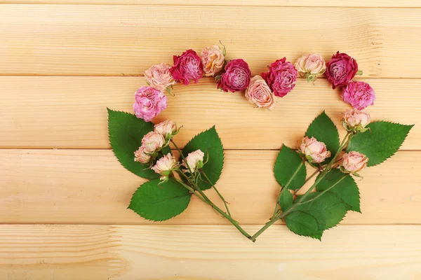 Coeur de belles fleurs sèches et feuilles vertes sur fond en bois — Photo