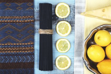 Peynir, siyah spagetti ve ahşap masa üstüne limon görüntüleyin