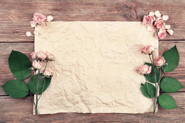 Dried roses on sheet of paper on wooden table, top view — Stock Photo, Image
