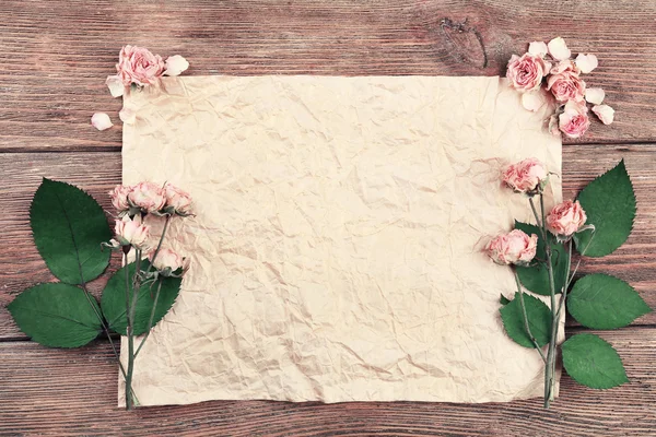 Gedroogde rozen op vel papier op houten tafel, bovenaanzicht — Stockfoto