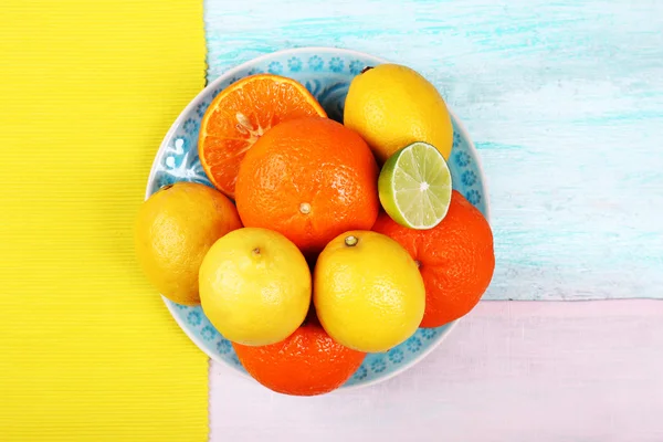 Mandarinen und Zitronen auf Teller auf hölzerner Tischplatte — Stockfoto