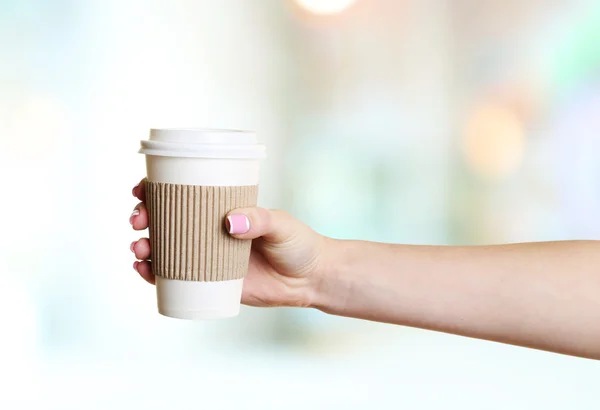 Mano femenina con taza de papel sobre fondo borroso brillante — Foto de Stock