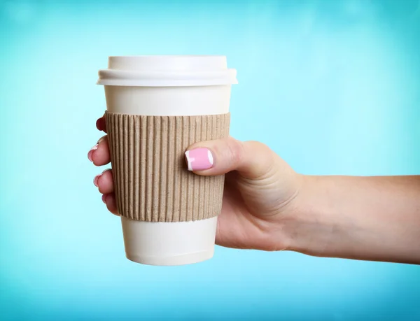 Mano femenina con taza de papel sobre fondo azul — Foto de Stock