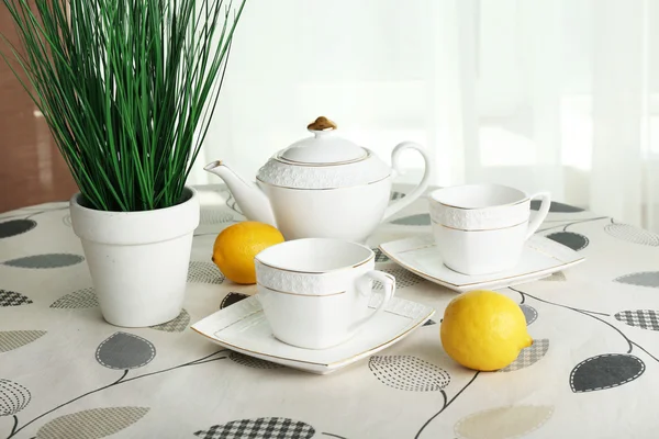 Planta verde con tetera, tazas y limones sobre mesa sobre fondo de cortinas — Foto de Stock