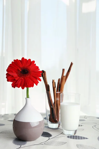 Rode gerbera bloem met glas melk en kaneelstokjes op tafel op gordijnen achtergrond — Stockfoto