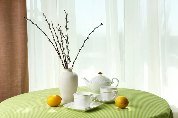 Willow twigs, teapot, cups and citrus on table on curtains background — Stock Photo, Image