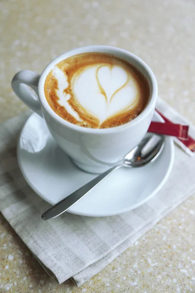 Cup of cappuccino with heart on foam on table in cafe — Stock Photo, Image