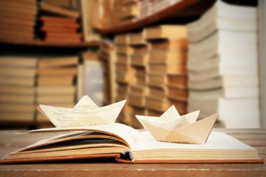 Kağıt tekne ile açık kitap kitap rafı arka plan üzerinde