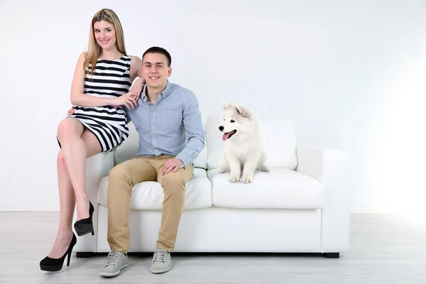 Couple and dog sitting on sofa, on light background — Stock Photo, Image