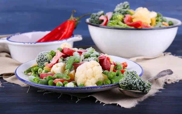 Verduras congeladas en plato sobre servilleta, sobre fondo de mesa de madera — Foto de Stock