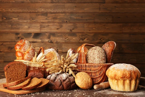 Different bread with ears in basket on wooden background — Stock Photo, Image
