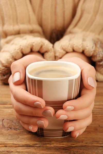 Kobiece ręce trzymając kubek kawy na drewnianym stole zbliżenie — Zdjęcie stockowe