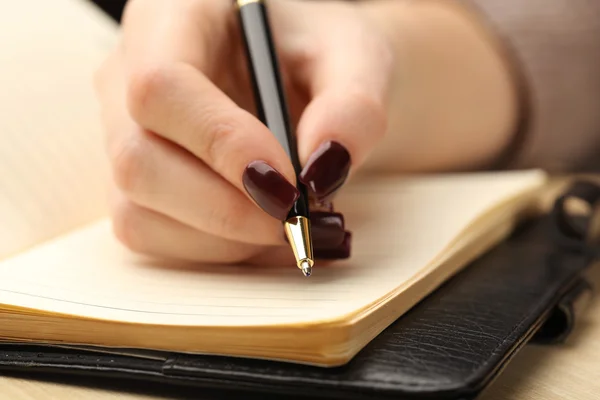 Kvinnlig hand skriva i dagboken av pen på träbord bakgrund — Stockfoto