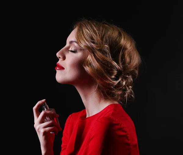 Hermosa joven con botella de perfume sobre fondo negro — Foto de Stock