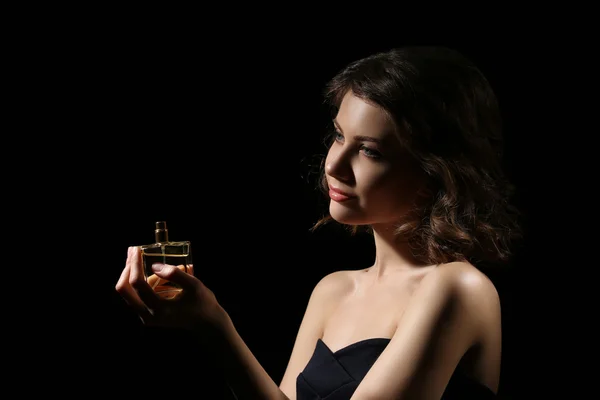 Hermosa mujer con frasco de perfume sobre fondo negro —  Fotos de Stock