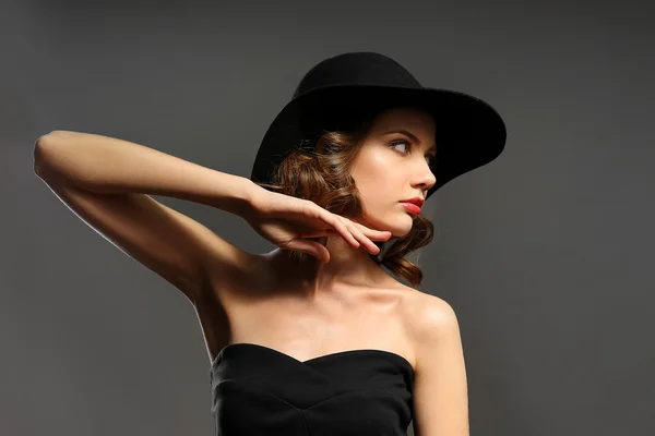 Retrato de modelo bonito em vestido preto e chapéu no fundo cinza — Fotografia de Stock