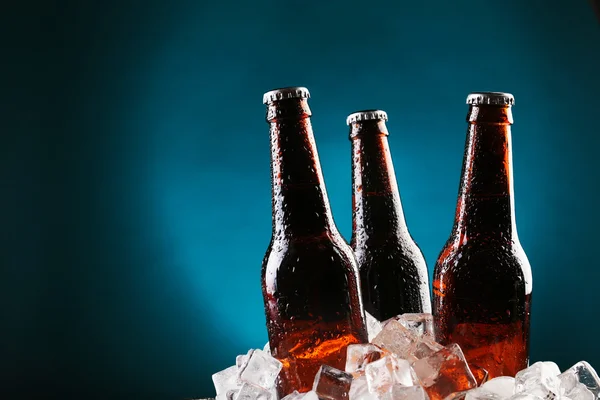 Glass bottles of beer in ice cubes on color background — Stock Photo, Image
