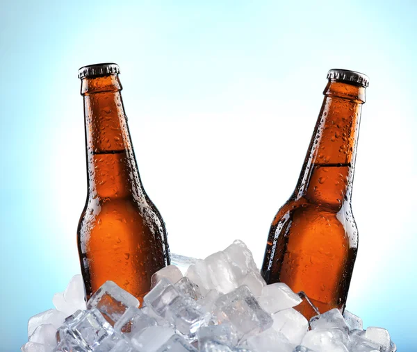 Glazen flessen bier in ijsblokjes op kleur achtergrond — Stockfoto