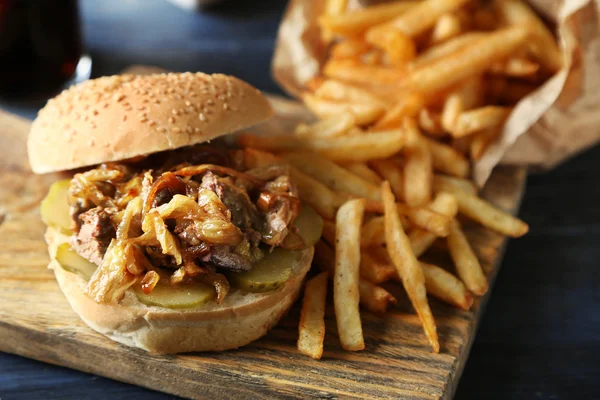 Tasty burger and french fries on plate, on wooden table background. Unhealthy food concept