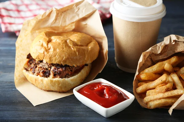 Νόστιμο burger και τηγανητές πατάτες στο πιάτο, σε ξύλινο τραπέζι φόντο. Έννοια ανθυγιεινών τροφίμων — Φωτογραφία Αρχείου