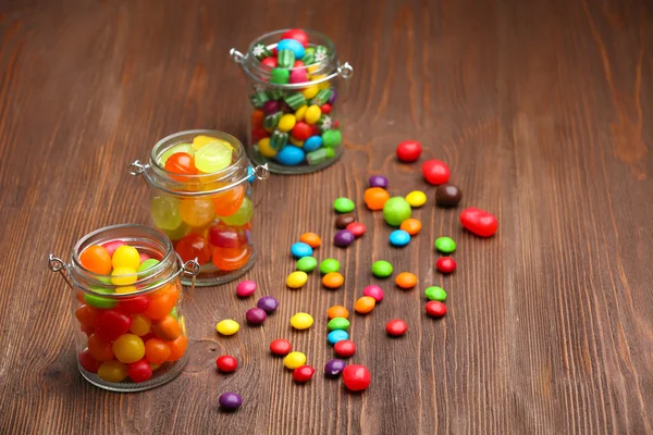 Bunte Bonbons in Gläsern auf Holzgrund — Stockfoto